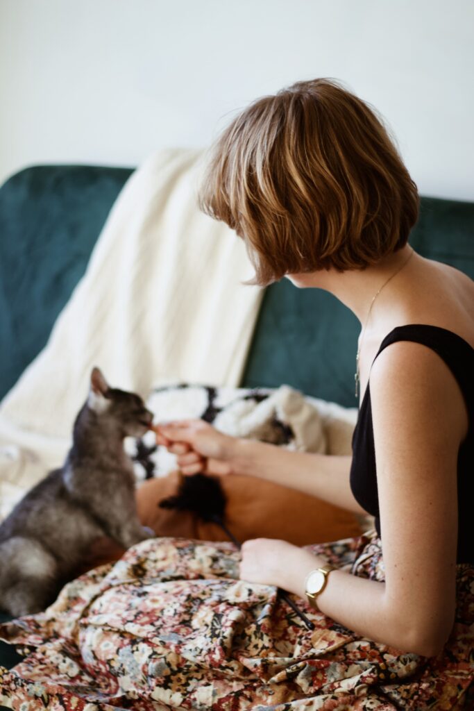 Izabela podająca kotce wyciskany przysmak. W drugiej dłoni trzyma wędkę z piórkami.