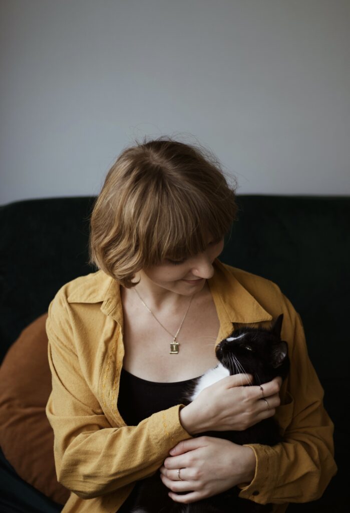 Izabela Stańczyk głaszcze kotkę Chloe. Ma na sobie miodową koszulę. Siedzą razem na kanapie i wpatrują się na siebie.